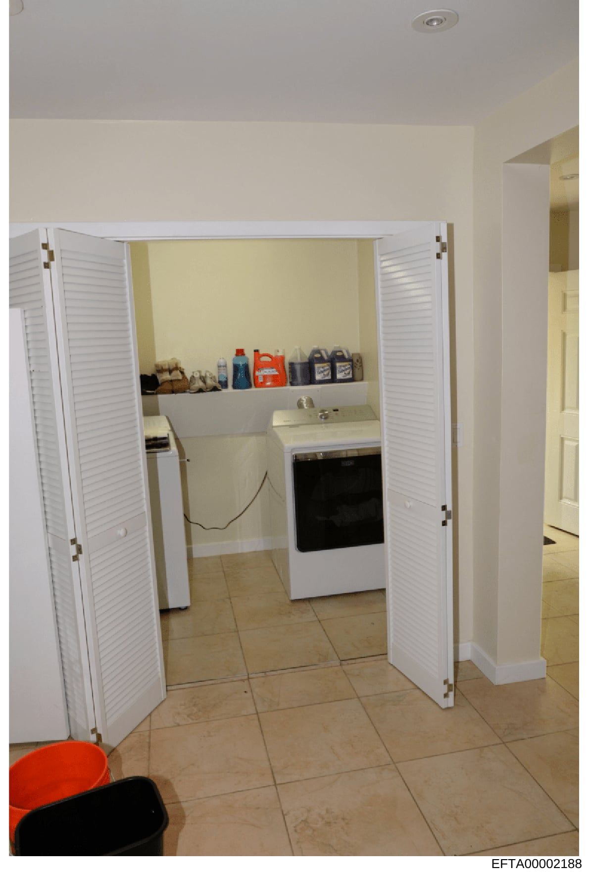 This is a photograph of a residential laundry room showing a washer and dryer unit, white louvered closet doors, shelving with cleaning supplies, and tan tile flooring. The image appears to be documentation of a property interior, likely from the Eps