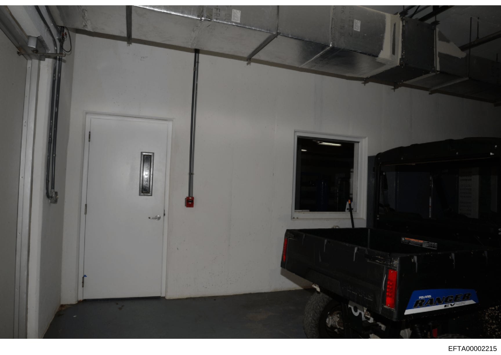 This is a photograph of an interior garage or storage facility showing a white-walled room with industrial features. A Polaris Ranger vehicle is visible on the right side of the image. The space appears to be part of a property associated with the in