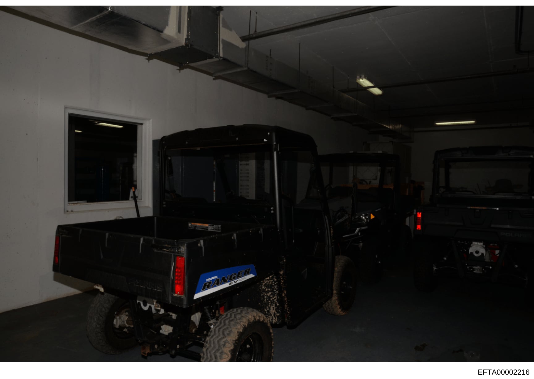 This photograph shows the interior of a garage or storage facility containing multiple dark-colored vehicles, including what appears to be a Range Rover (visible blue nameplate) in the foreground. The facility features industrial ceiling fixtures, fl