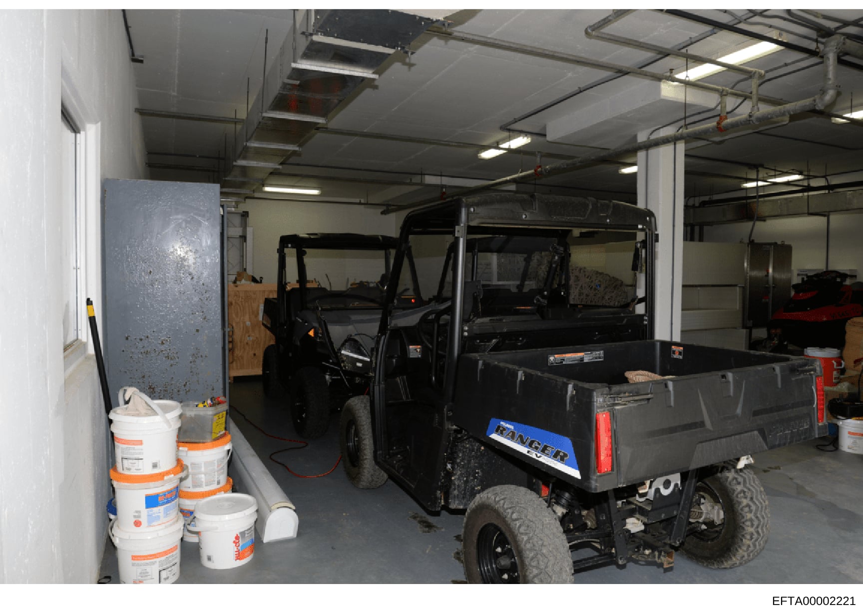 This photograph shows an interior storage garage or warehouse space containing multiple vehicles, including what appears to be utility vehicles and a Ford Ranger pickup truck, along with various stored supplies and buckets. The image documents the co