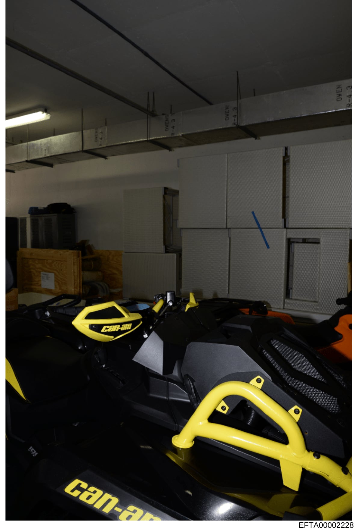 This photograph documents the interior of a storage facility containing multiple Can-Am branded all-terrain vehicles (ATVs) in yellow and black colors, along with wooden shipping crates and various equipment. The image appears to be evidence document