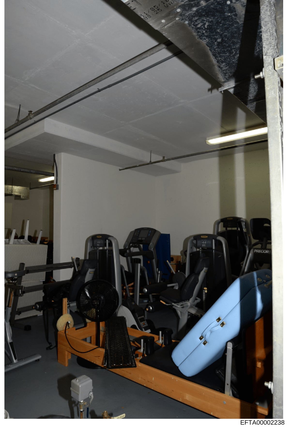 This is an evidence photograph showing the interior of a room containing multiple exercise machines and fitness equipment, including stationary bikes and other gym equipment with black and orange coloring. The image documents the condition and conten