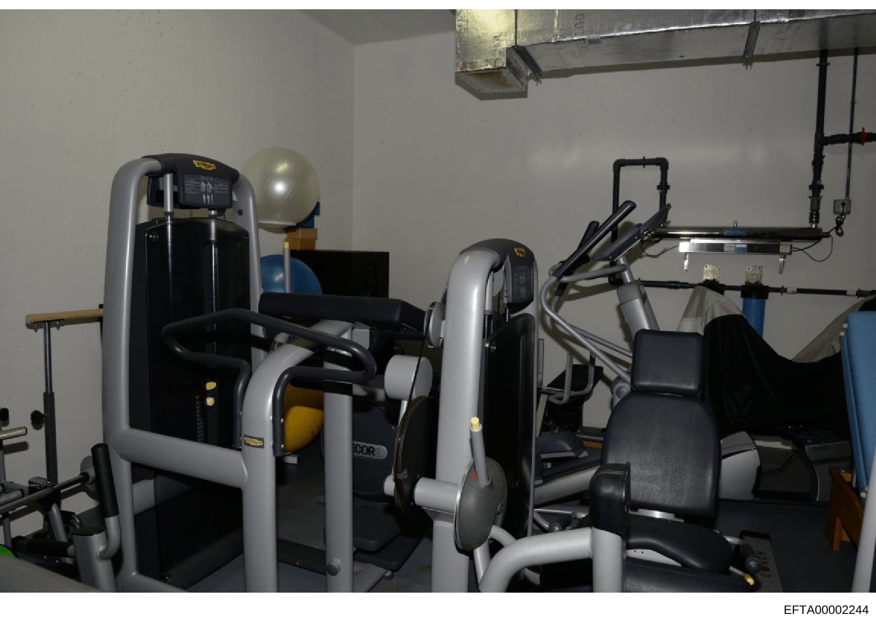 This photograph shows the interior of a gymnasium or fitness facility containing multiple pieces of exercise equipment including weight machines, an exercise bike, and treadmill-style equipment. The image appears to be from an evidence collection rel
