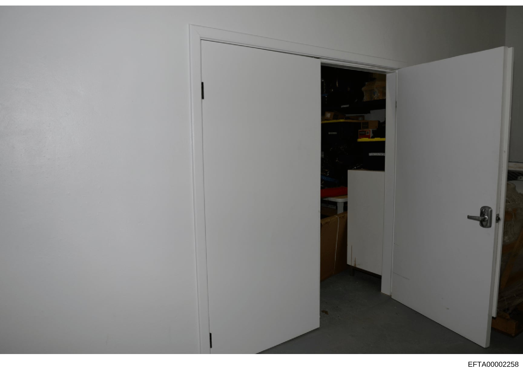 This photograph shows an interior space featuring two white double doors in an open position, revealing a darkened room or storage area with various items visible inside. The image appears to be documentation of a property's interior layout, potentia