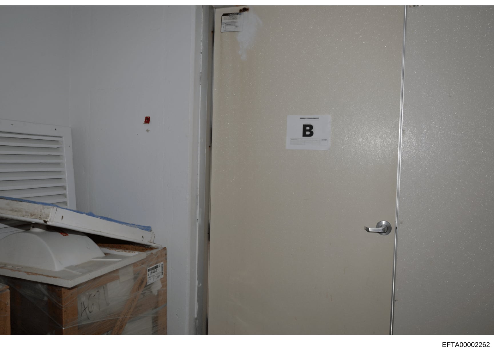 This is an evidence photograph showing the interior of a room, likely from a property search or seizure. The image displays a door marked with an evidence label 'B', a wall-mounted ventilation unit, an electrical outlet, and what appears to be wooden