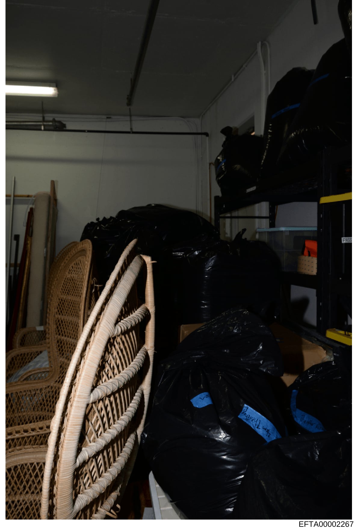 This is an evidence photograph showing an interior storage space containing multiple sealed black plastic bags or containers labeled with blue tape markings, woven rattan chairs, rolled materials, and various storage items. The sealed containers and 