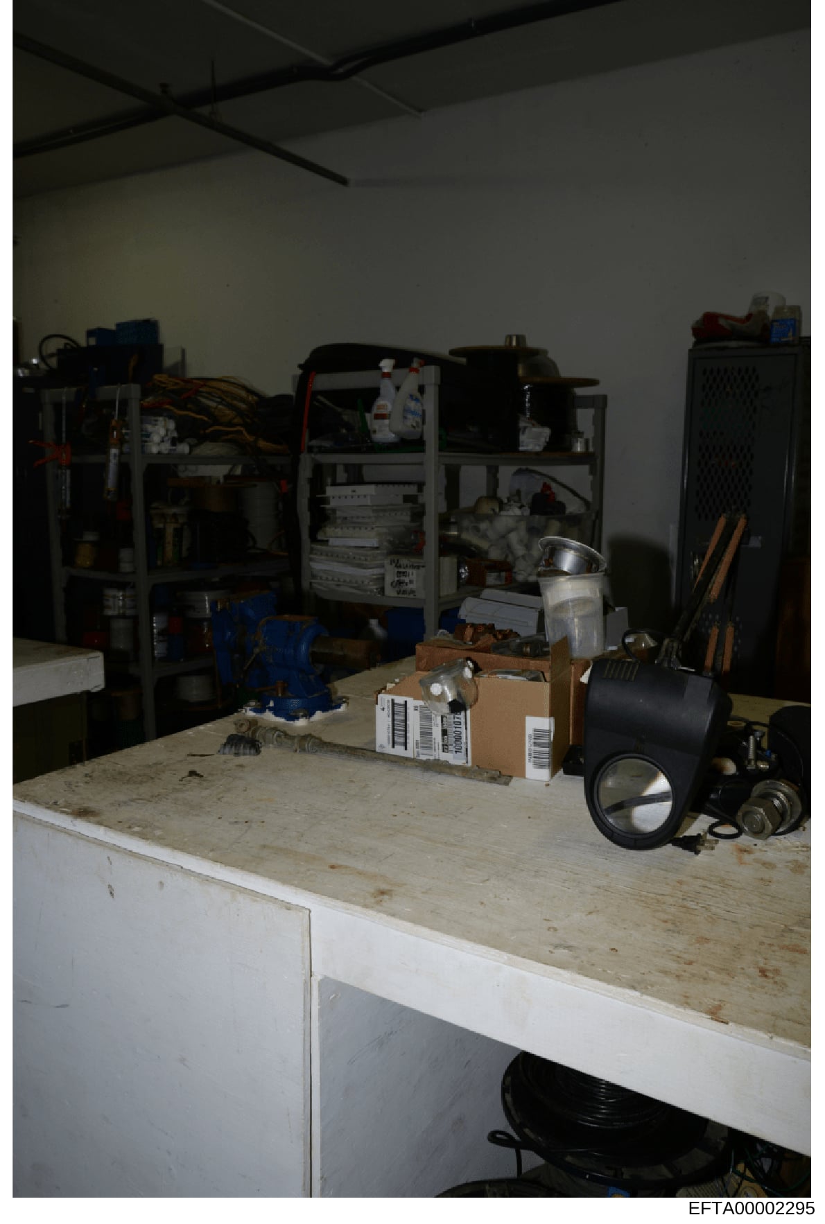 This is an evidence photograph showing an interior room containing various electronic equipment, networking hardware, boxes, tools, and storage items. The room appears to be a technical or server space with metal shelving units holding computer equip