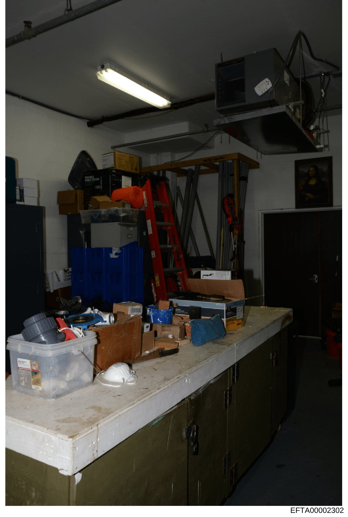 This is an evidence photograph showing the interior of a storage or maintenance room, likely from an Epstein property. The image captures various items stored on shelves and work surfaces, including tools, containers, cleaning supplies, and household