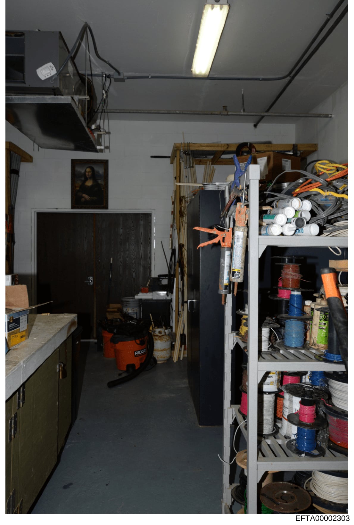 This is an interior photograph of a storage or workshop space containing tools, supplies, and miscellaneous items organized on shelves and hanging storage. The room features utility shelving, an orange power tool (wet/dry vacuum), paint cans, tools, 