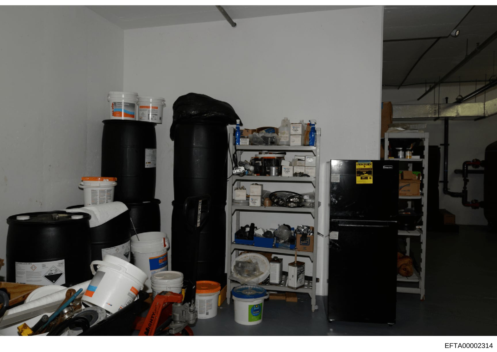 This photograph shows an interior storage or maintenance space containing various chemical containers, cleaning supplies, tools, and equipment organized on shelves and the floor. The image appears to be evidence documentation from a property search o