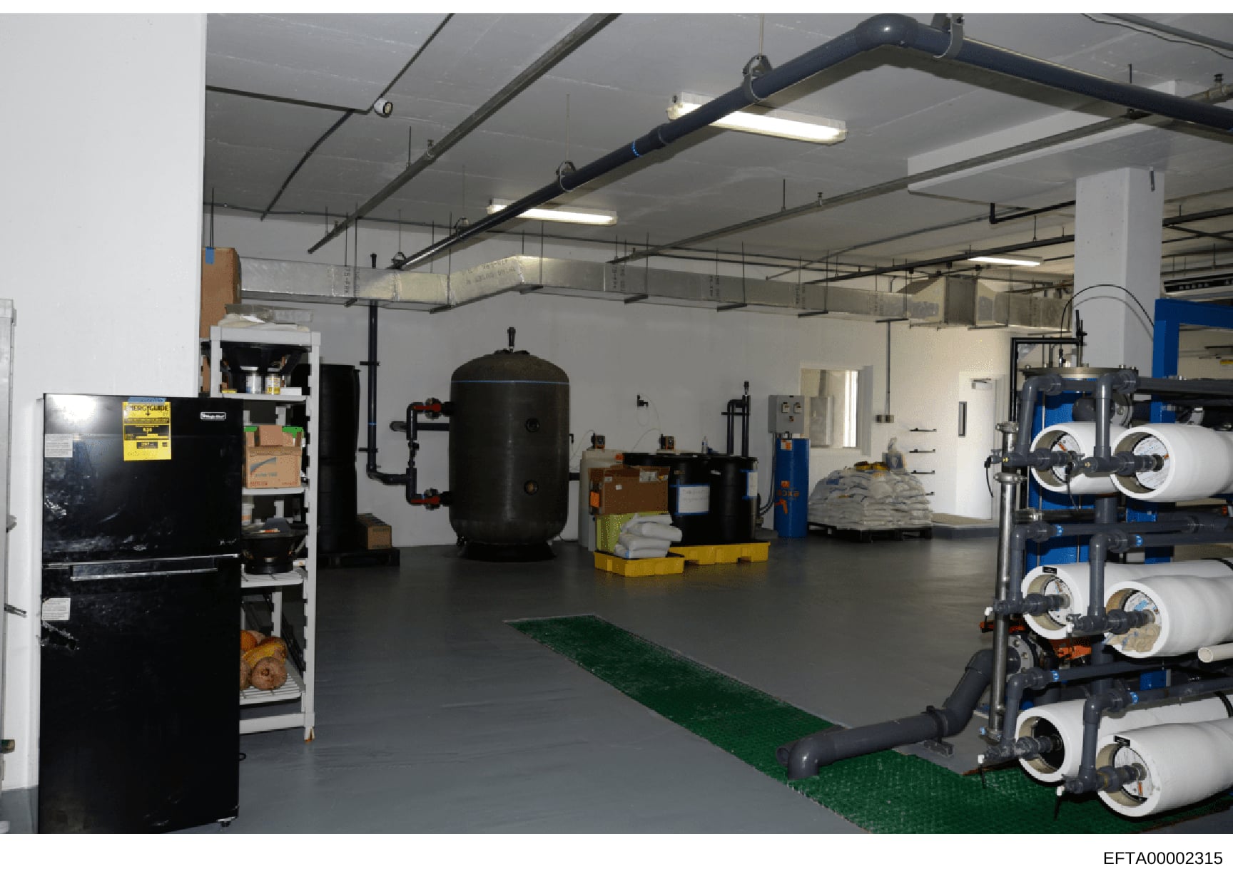 This is a photograph of an industrial or commercial mechanical/equipment room, likely from a large property. The space contains HVAC systems, water storage tanks, piping infrastructure, and various maintenance equipment. The image appears to be part 