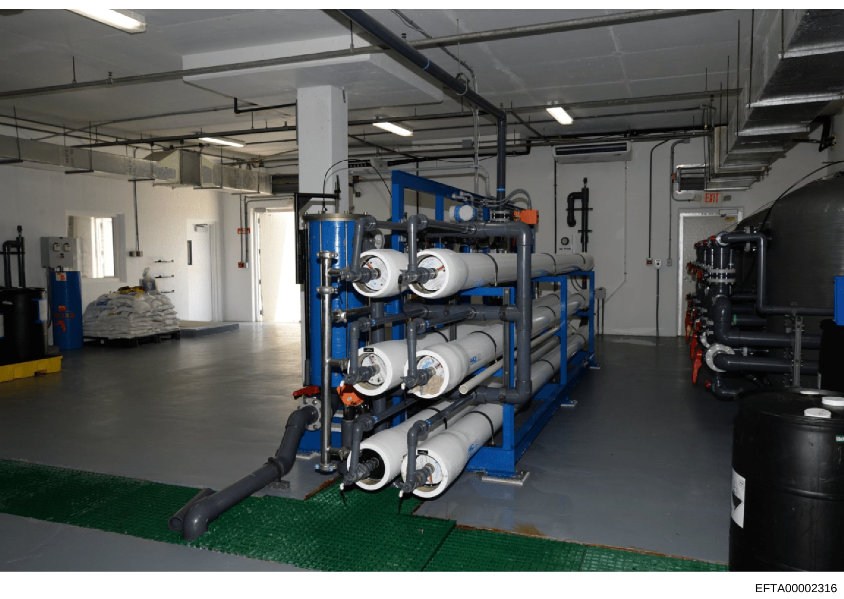 This photograph shows the interior of an industrial water treatment or filtration facility featuring large-scale reverse osmosis or filtration equipment. The image captures multiple blue-framed membrane filter units with cylindrical cartridges arrang