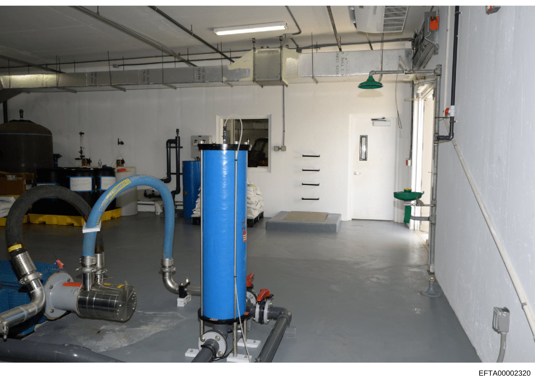This is a photograph of an industrial or commercial mechanical/utility room, showing water treatment or HVAC equipment including blue cylindrical tanks, pumps, piping systems, and various mechanical infrastructure. The image appears to be evidence do