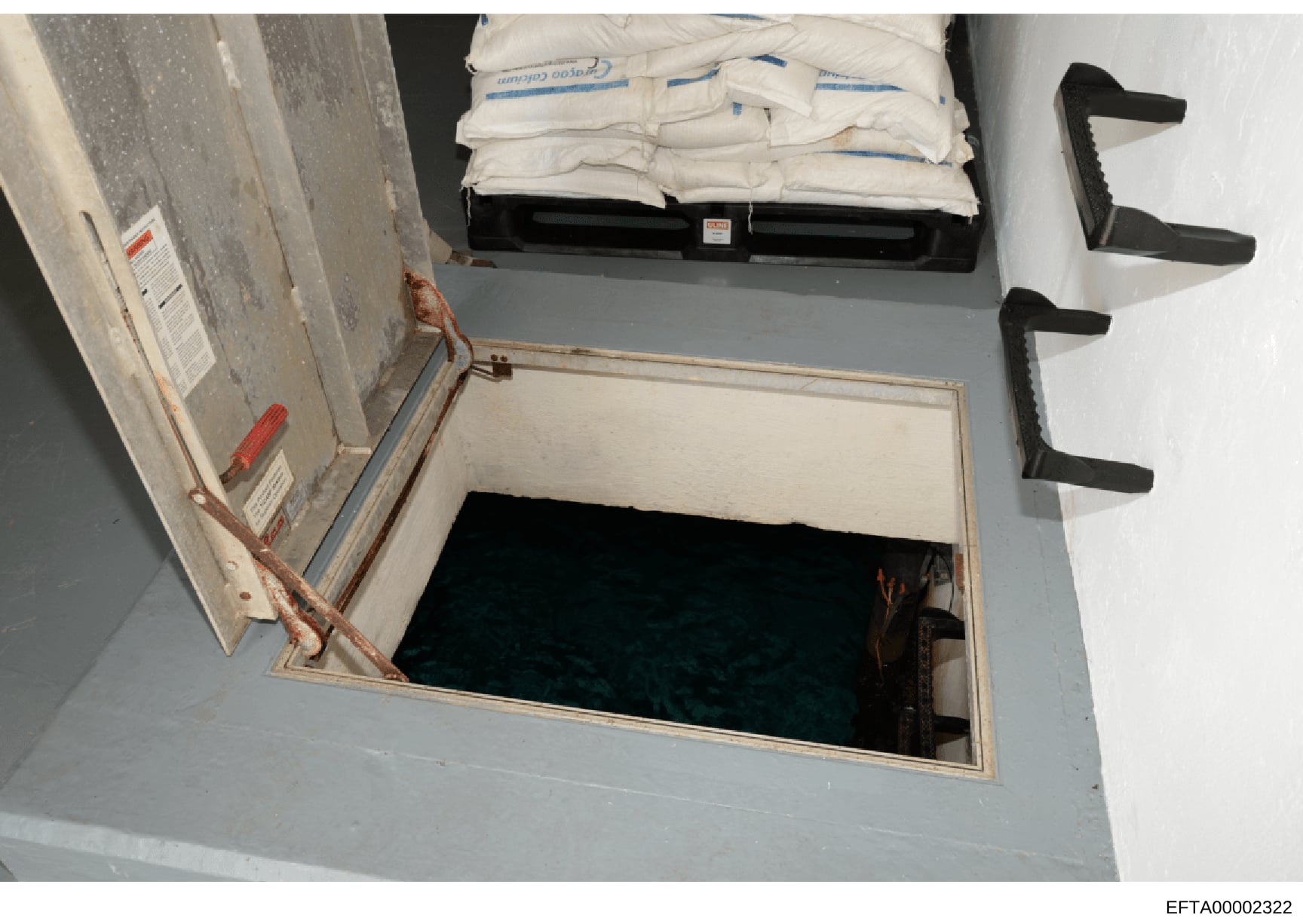 This is an evidence photograph showing an open attic or overhead storage access point containing white plastic bags with blue labeling stacked on a black tray, along with black handles or brackets visible on the right side. The space appears to be pa