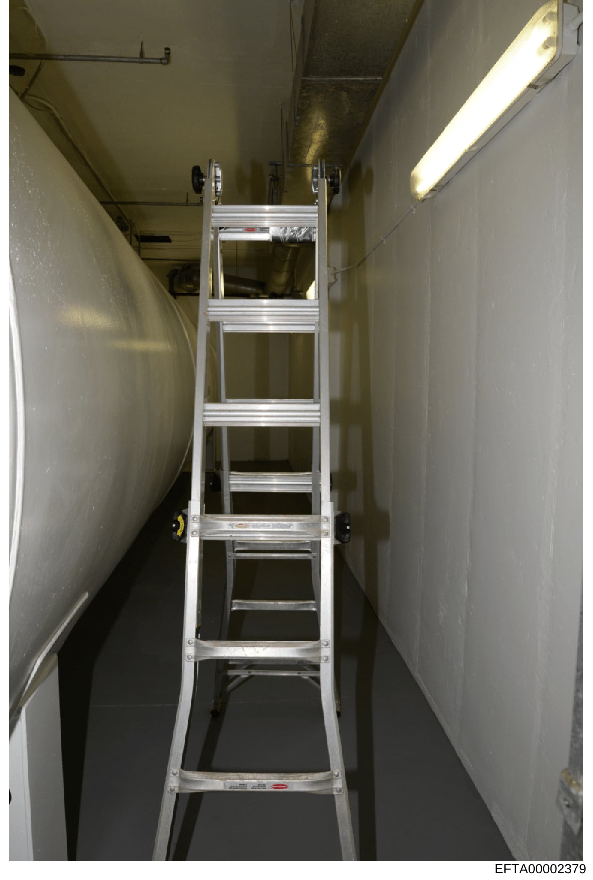This is an evidence photograph showing the interior of a narrow hallway or corridor in what appears to be a basement or utility area, with an aluminum extension ladder positioned in the center. The space features plain white walls, fluorescent lighti