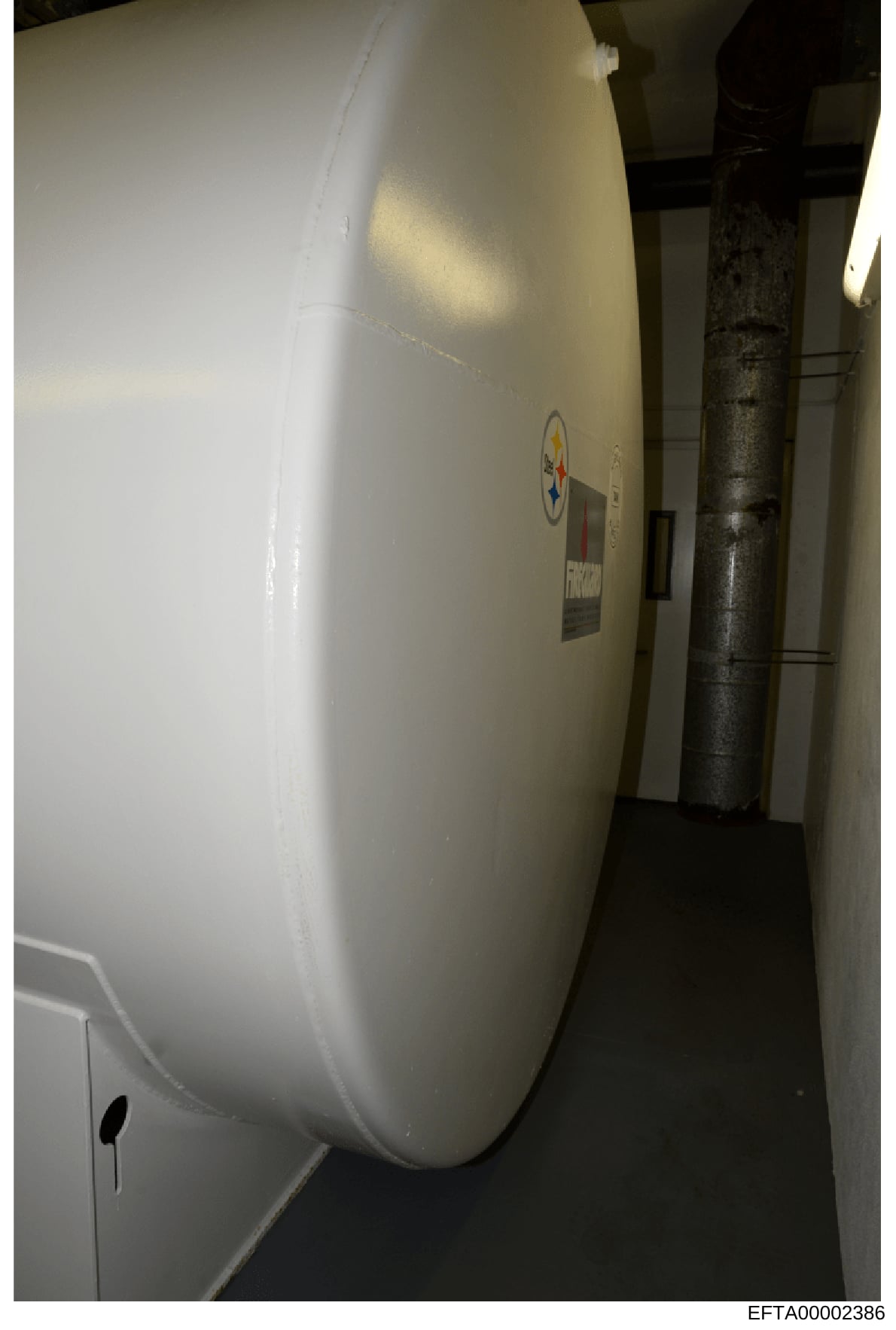 This photograph shows the interior of a narrow corridor or utility space containing a large, curved white tank or vessel. The image appears to be property documentation, possibly from an Epstein-owned residence or facility, showing mechanical or stor