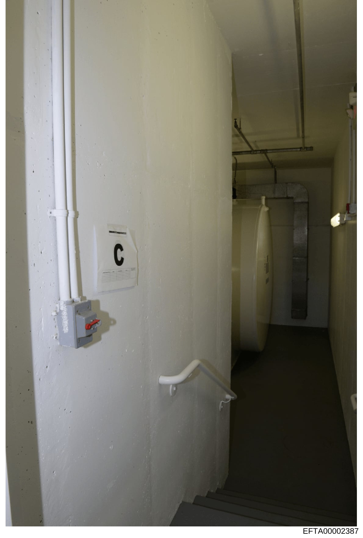 This is an evidence photograph showing an interior hallway or narrow corridor space, likely from one of Epstein's properties. The image captures white painted walls, electrical wiring, a thermostat marked 'C', a wall-mounted electrical panel with a r