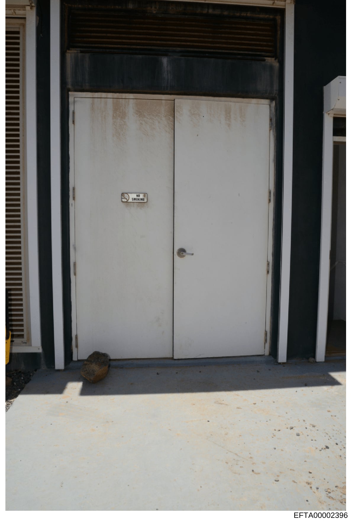 This is an evidence photograph showing a double-door entrance with a visible 'No Smoking' sign mounted on the doors. The doors appear worn with stains and discoloration on their surfaces. The image documents the exterior condition of what appears to