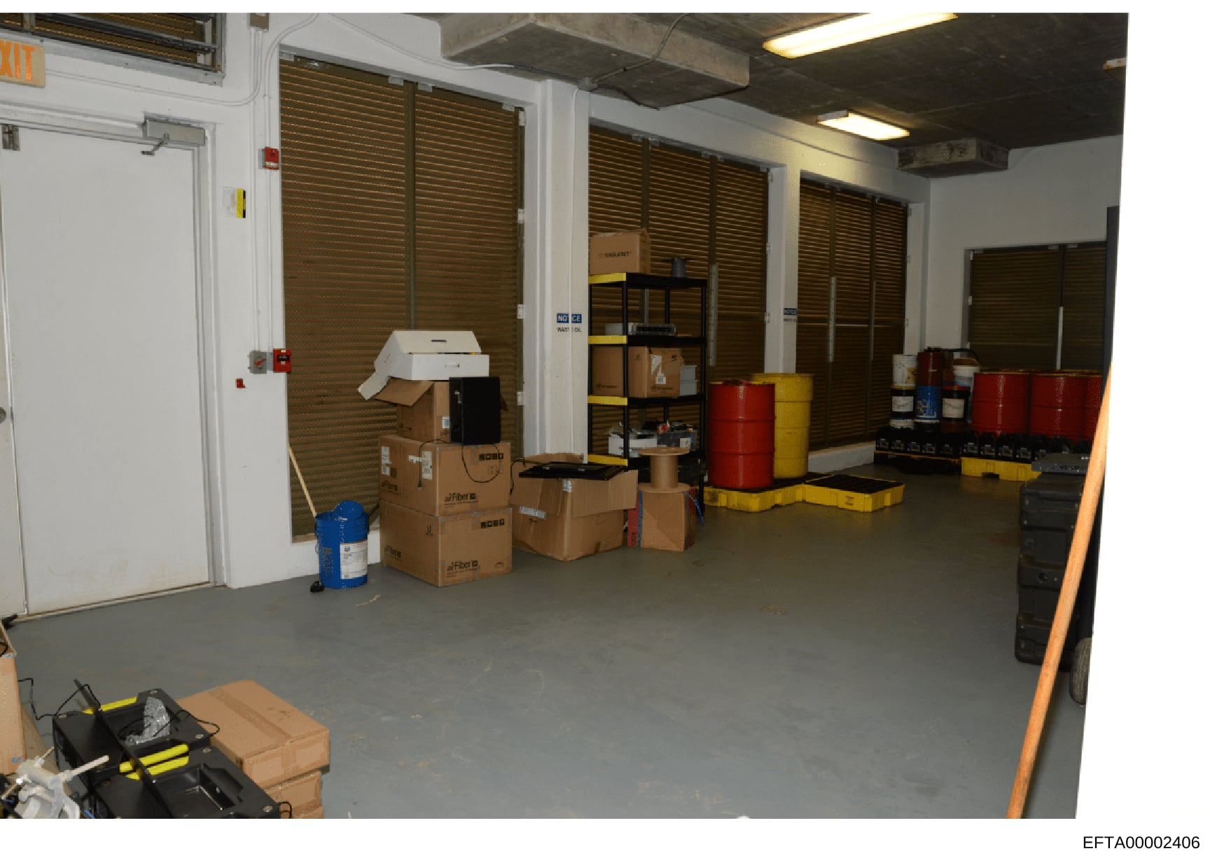 This is a photograph of an industrial or commercial storage facility showing a climate-controlled storage unit containing multiple cardboard boxes, red and yellow drums or containers, shelving units, and various equipment. The space appears to be par