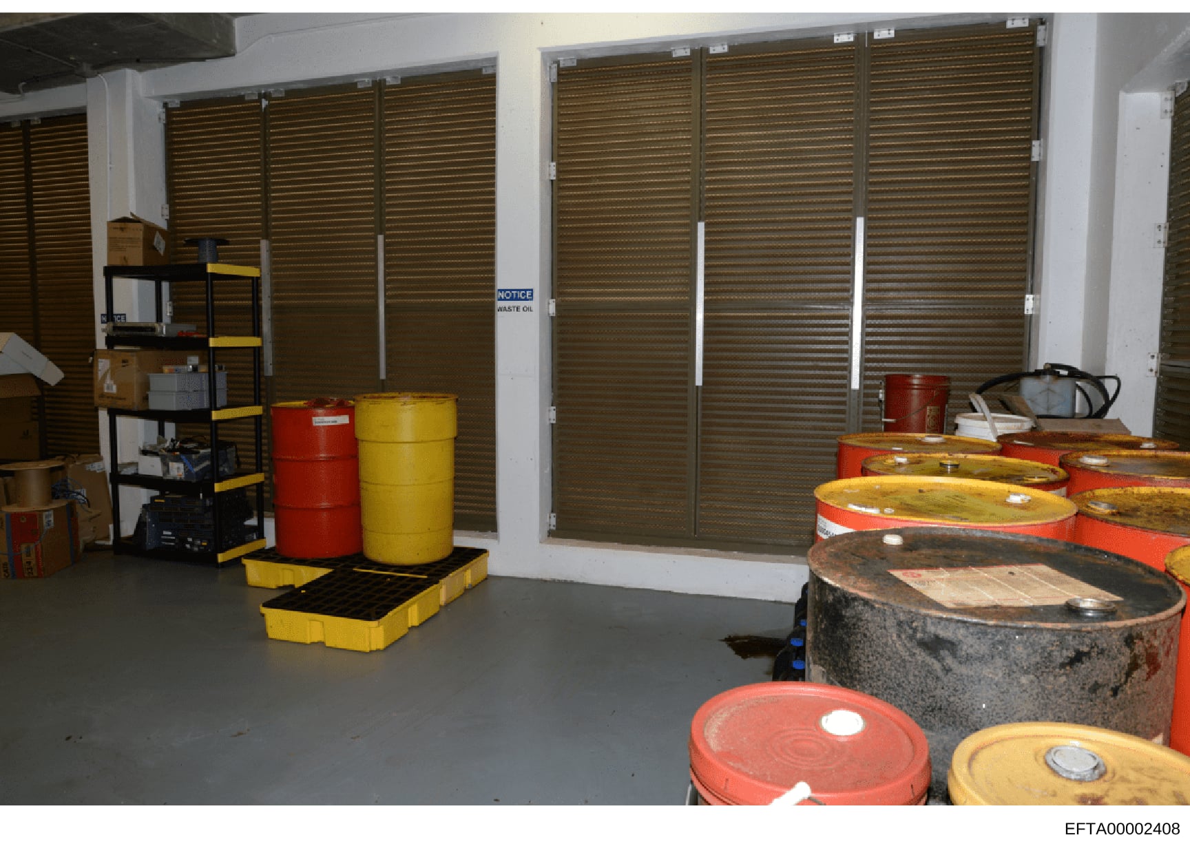This photograph shows an interior storage area containing multiple industrial drums (red and yellow barrels), shelving units, and hazard containment equipment. A 'NOTICE' sign referencing waste oil is visible on the wall. The space appears to be a ba