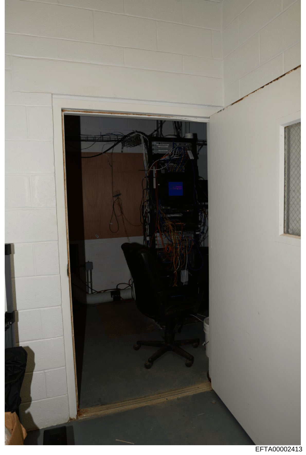 This photograph shows an interior room or closet space containing computer equipment, networking infrastructure, and various cables. The image appears to be from a property search or evidence documentation, showing a workspace with a desk chair, elec