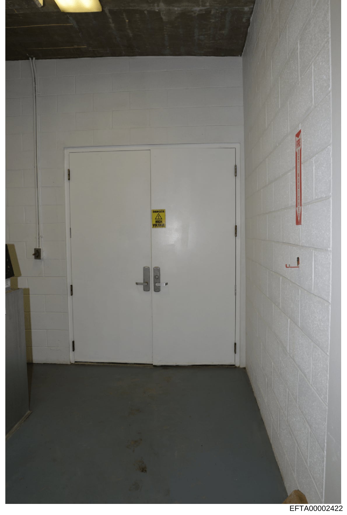 This is an evidence photograph showing an institutional or commercial interior hallway with white subway tile walls, a concrete floor, and a set of double white doors with electronic locks. A yellow 'Danger' warning sign is visible on the doors, and 