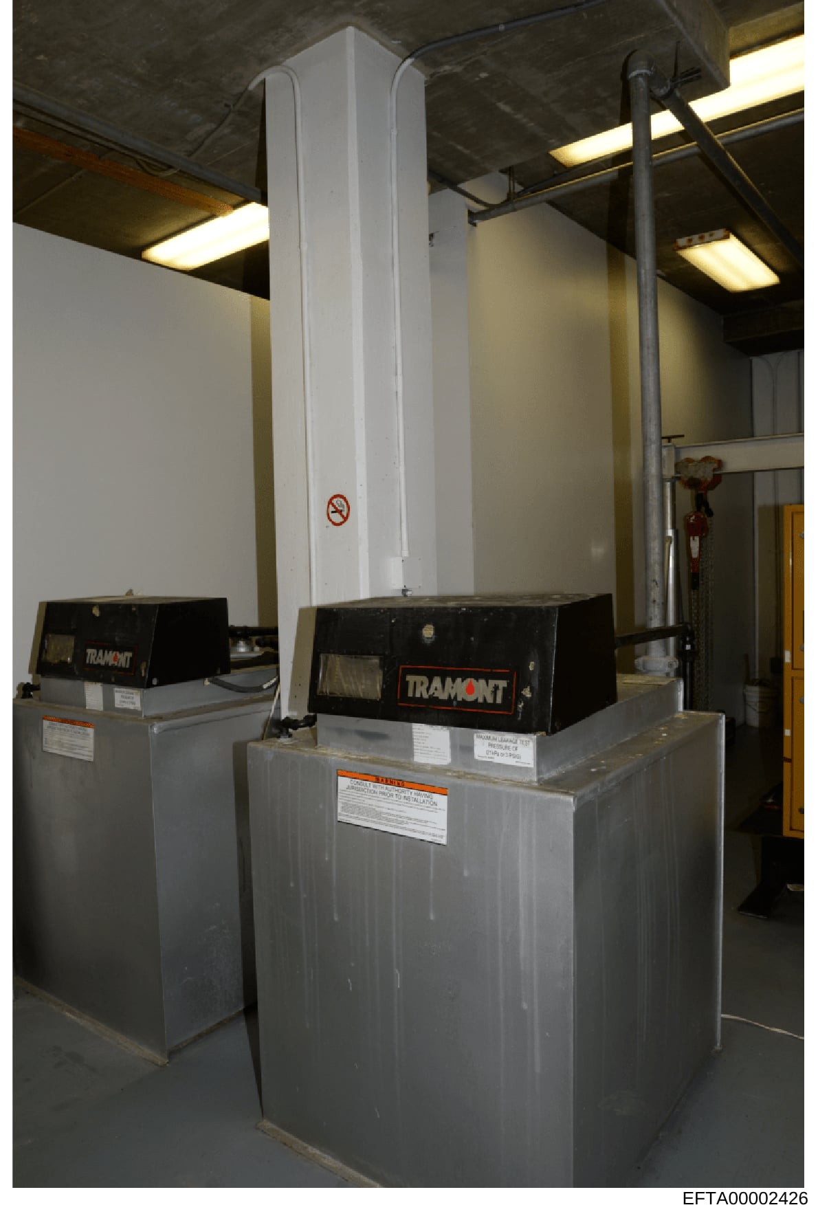 This is a photograph of industrial HVAC equipment (two Tramont units) installed in what appears to be a basement or mechanical room of a property. The image shows commercial heating/cooling infrastructure with a tall white vertical duct or chimney, m