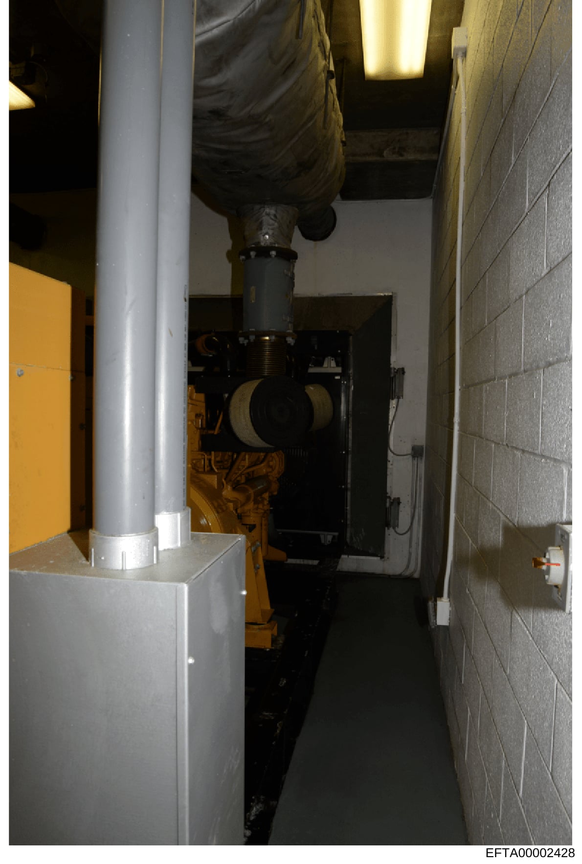 This is an evidence photograph showing the interior of a narrow mechanical or utility room containing industrial equipment. The image displays a large yellow and black generator or similar mechanical apparatus, a gray support column, concrete block w