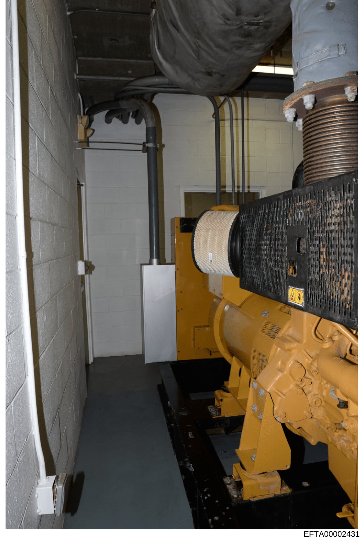 This photograph documents the interior of a generator or mechanical room, showing industrial equipment including a large yellow diesel generator with black radiator panel, storage tanks, piping systems, and concrete block walls. The image appears to 
