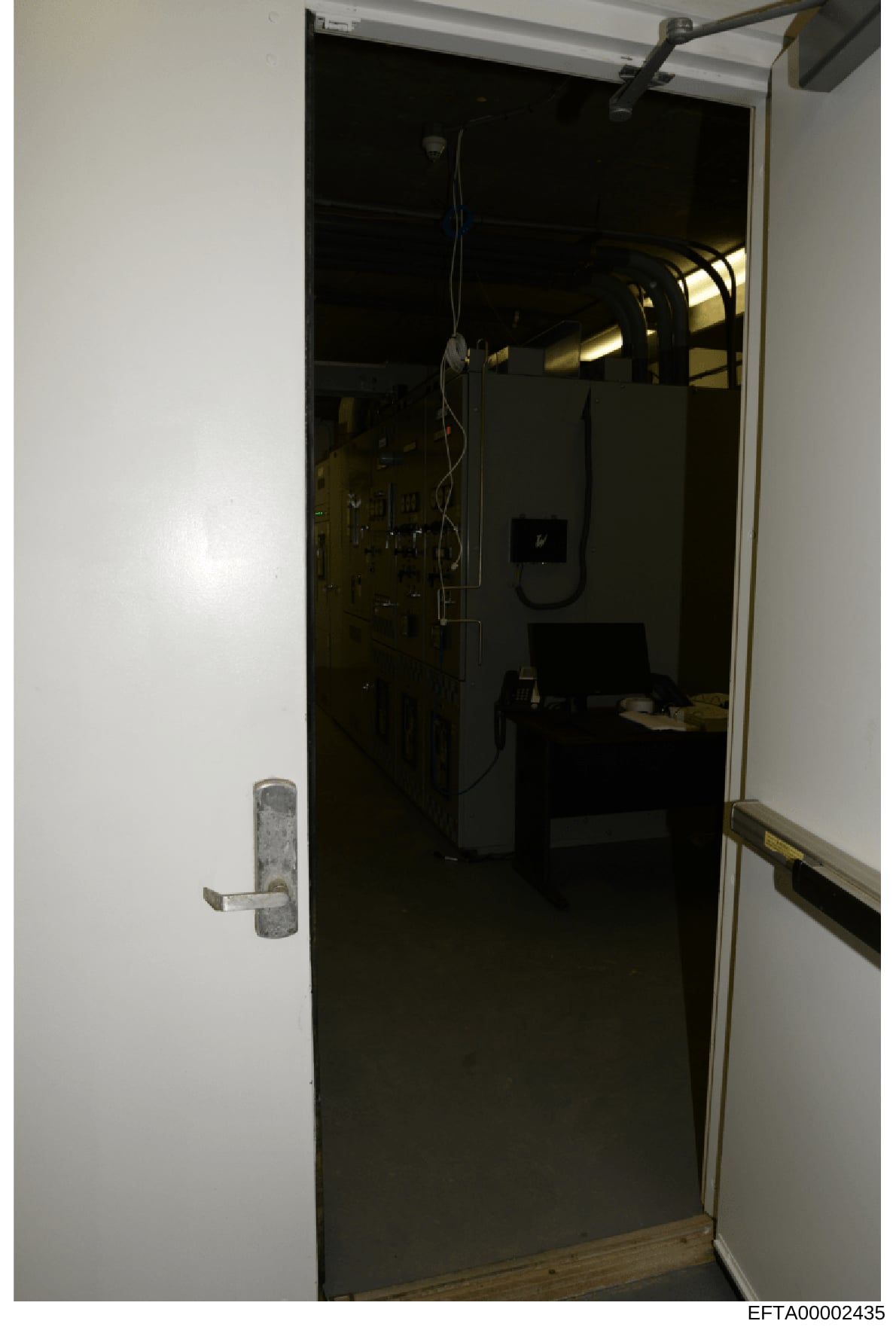 This is a photograph of an interior room or closet space showing various equipment installations, including what appears to be mechanical systems, electrical components, and a secured door with a metal handle. The image was taken as evidence document