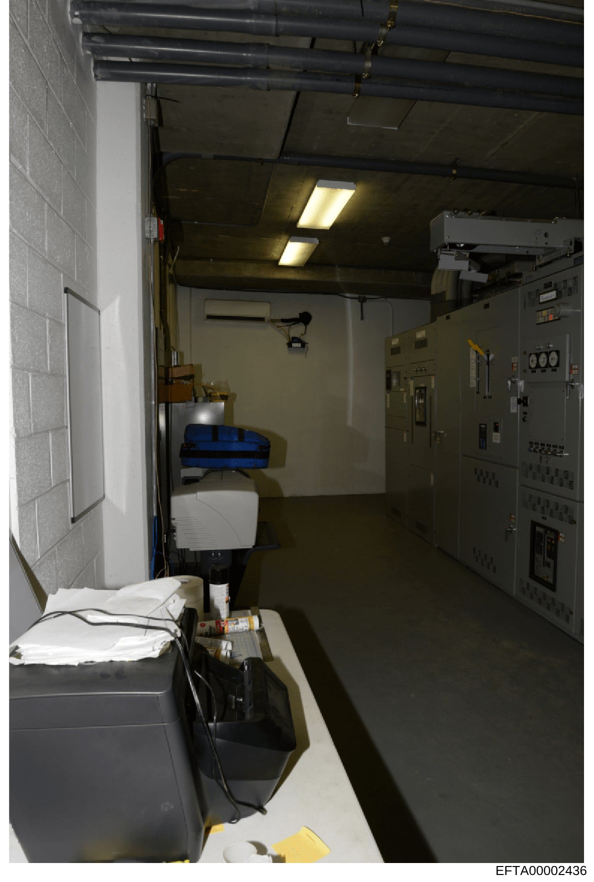 This is an evidence photograph showing the interior of a utility or mechanical room, featuring electrical panels, control systems, and storage equipment. The image documents the infrastructure of what appears to be an institutional or commercial buil