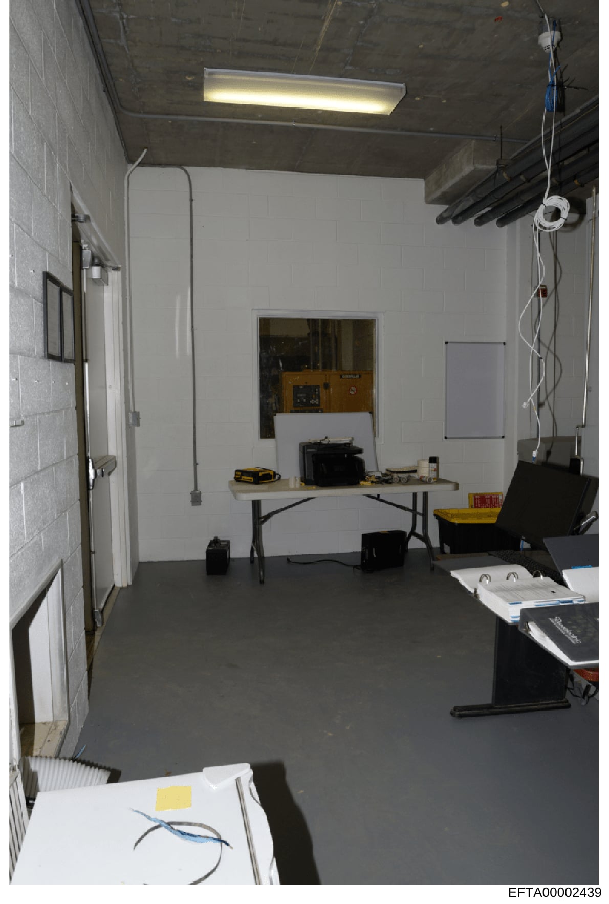 This is an evidence photograph showing the interior of a basement or utility room containing a folding work table, various tools and equipment, exposed ceiling infrastructure, and electrical wiring. The space appears to be used for storage or work pu