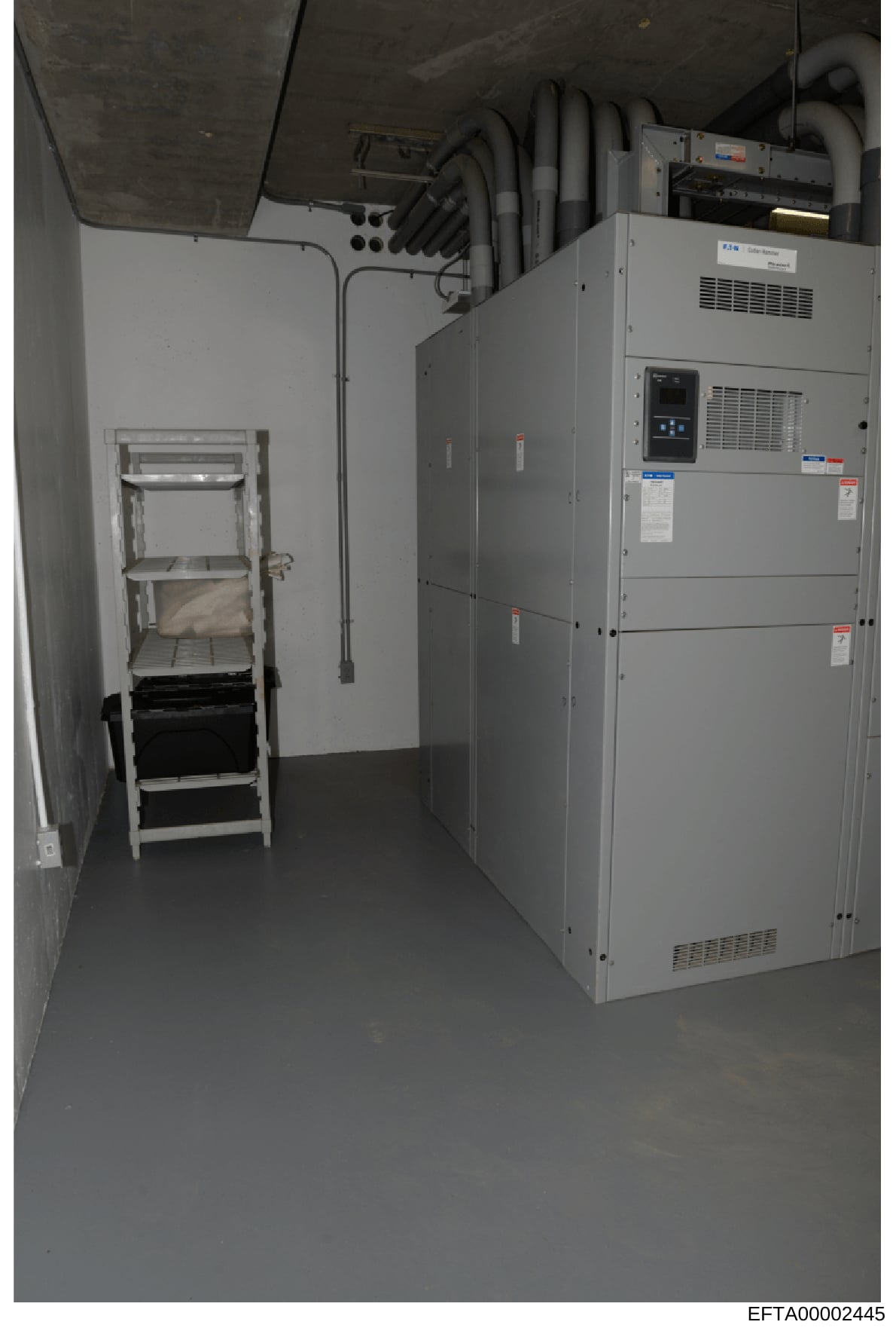 This photograph documents a utility/mechanical room within a property, showing industrial heating, ventilation, and air conditioning (HVAC) equipment along with electrical infrastructure. The image appears to be evidence documentation of building sys