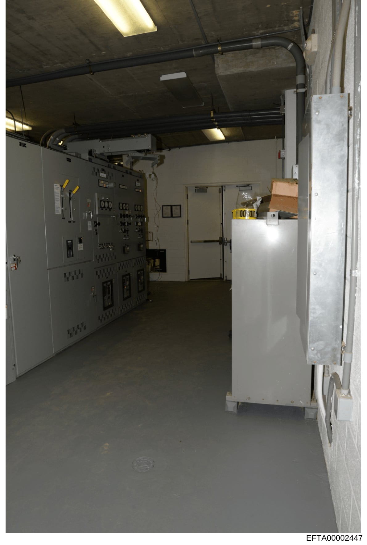 This is an evidence photograph showing the interior of an industrial or utility control room, featuring electrical panels, circuit breakers, piping infrastructure, and storage areas. The image appears to be documentation of a building's mechanical or