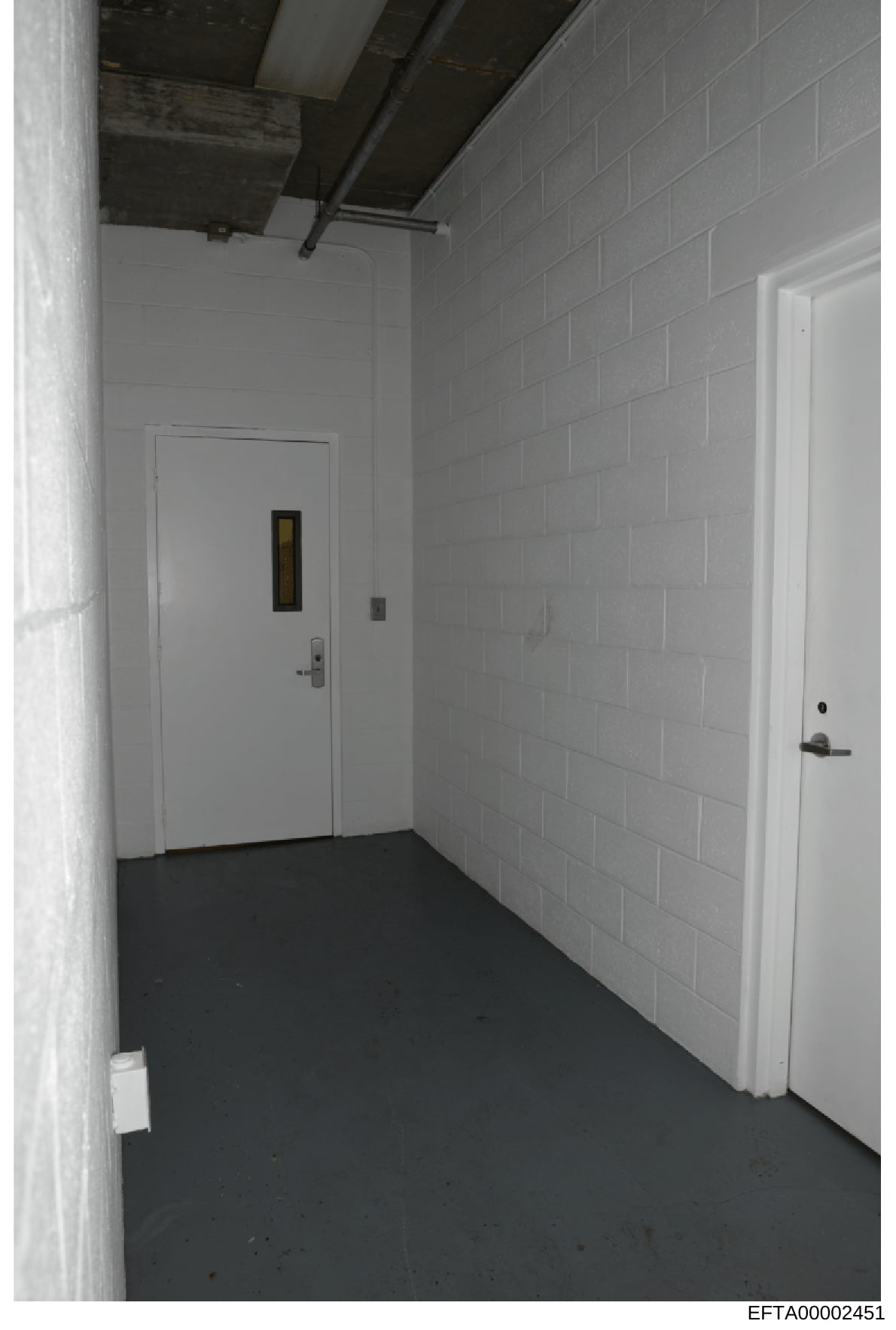 This is an evidence photograph showing an interior hallway or basement corridor with white cinderblock walls, a dark floor, and multiple white doors. The image appears to be from a property inspection or evidence documentation, likely from one of Eps