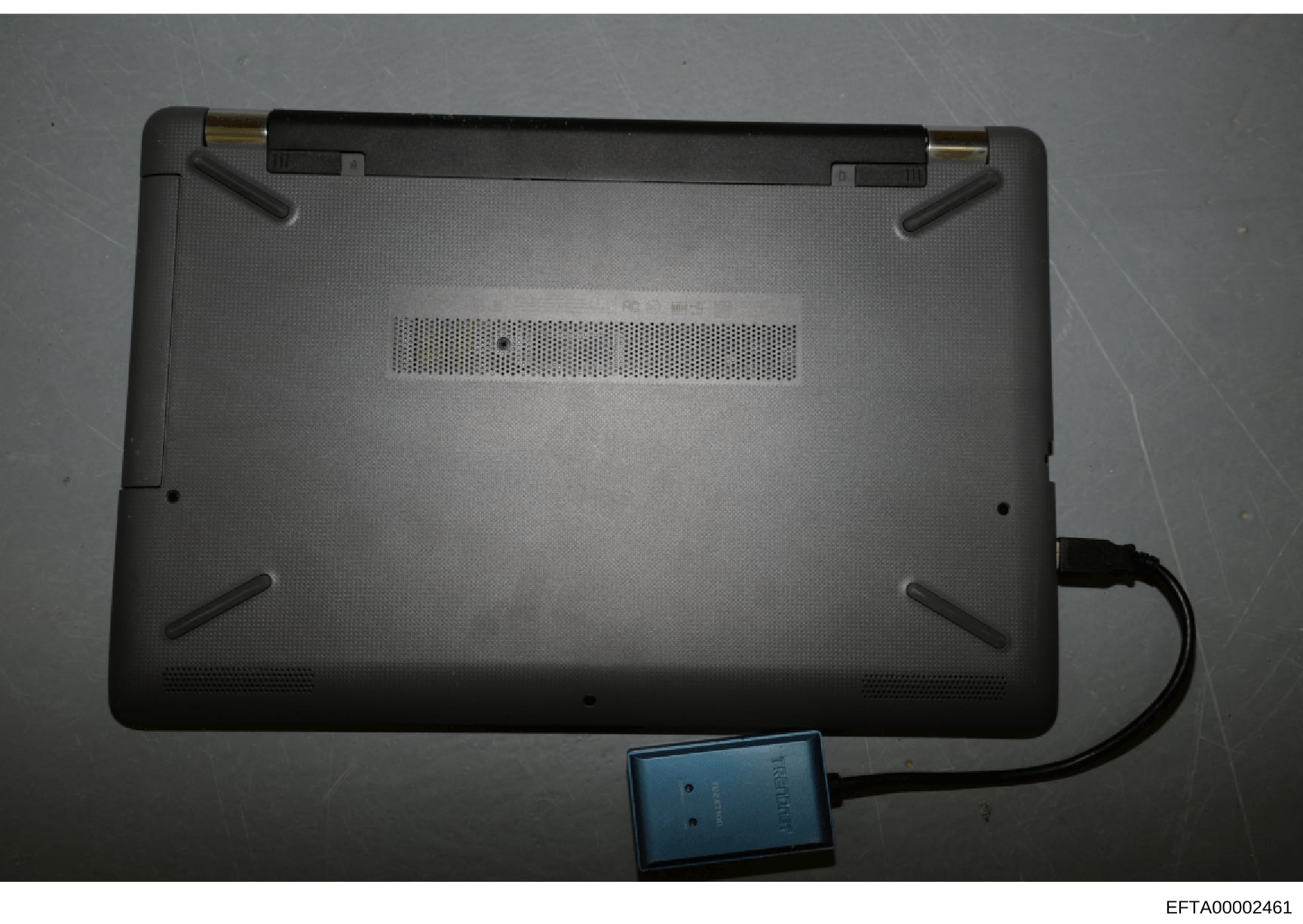 This is a photograph of the underside of a laptop computer, showing the bottom panel with ventilation grilles and what appears to be an external storage device or drive connected via cable. The image is marked as evidence (EFTA00002461) in the Jeffre