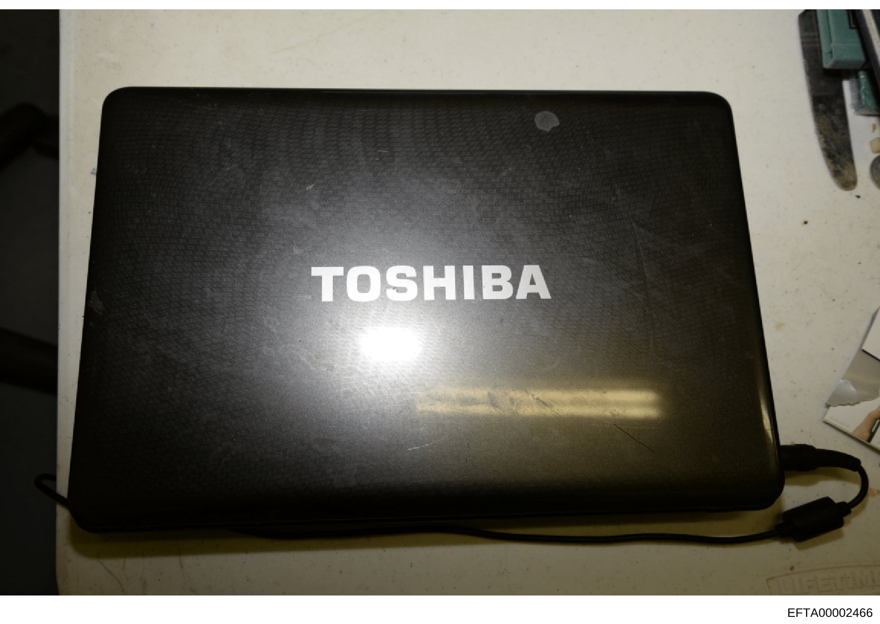 This is a photograph of a Toshiba laptop computer, likely seized as evidence during the investigation. The image shows the closed lid of the device with the Toshiba branding visible. The laptop's condition and contents may be relevant to the investig