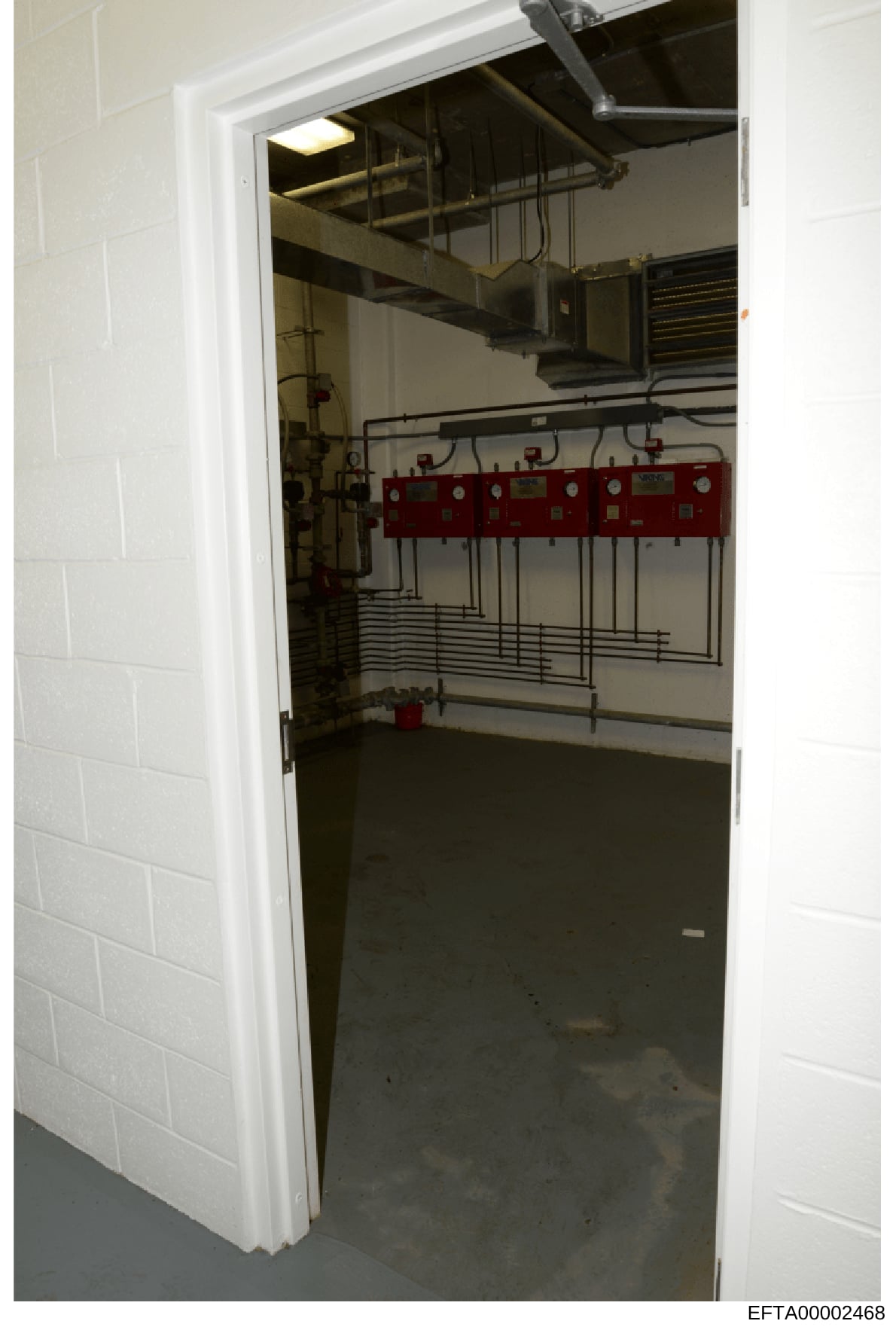 This photograph shows the interior of an electrical or utility room, likely from one of Epstein's properties, featuring fire suppression equipment, electrical panels, and HVAC systems. The room contains red fire safety modules mounted on the wall and