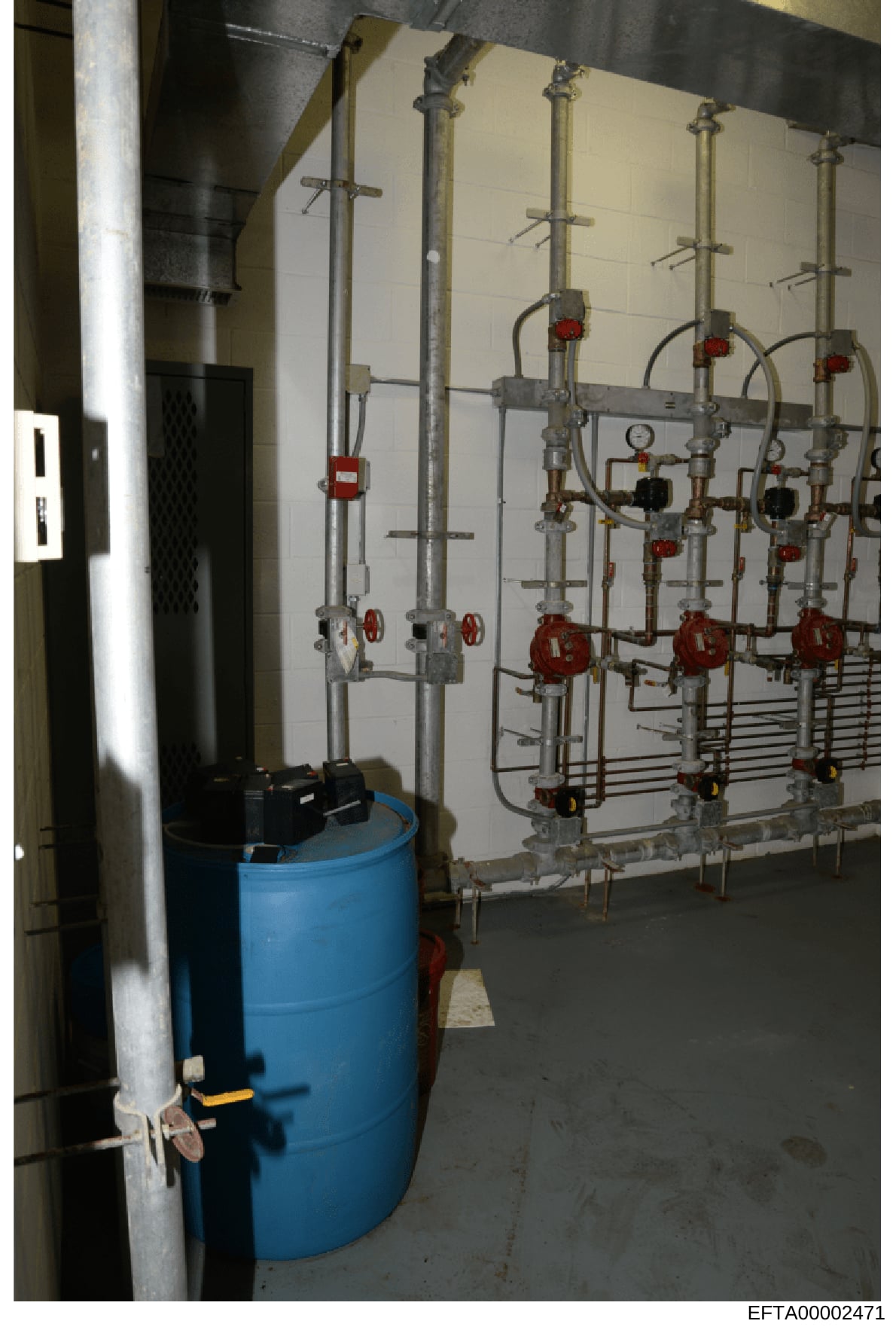 This photograph shows the interior of a mechanical systems room, likely part of building infrastructure at one of Epstein's properties. The image displays an extensive network of brass and metal piping with multiple red valves, gauges, and control me