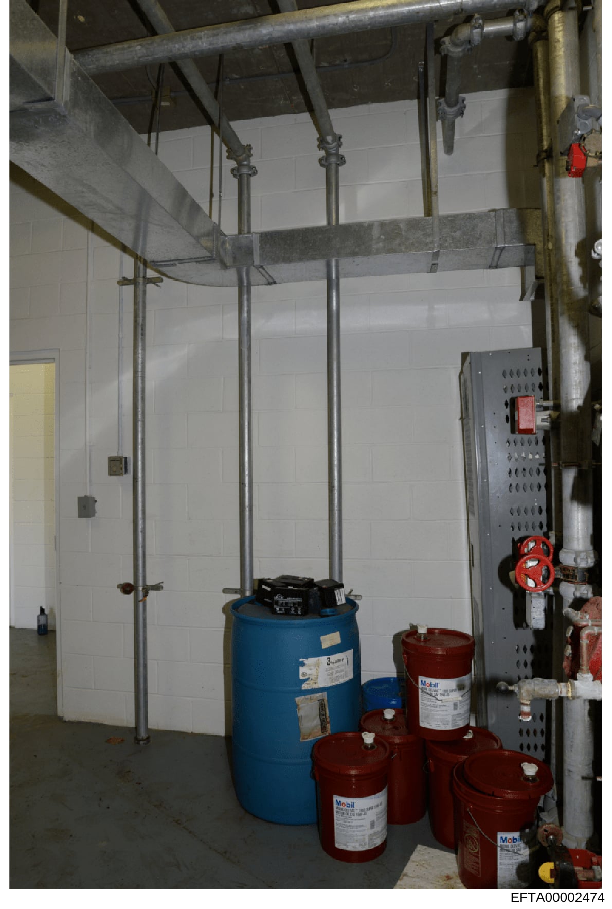 This is an evidence photograph showing the interior of a mechanical or utility room, featuring industrial piping, HVAC or water system components, and multiple storage tanks (one blue, several red Mobil-branded containers). The image documents the in