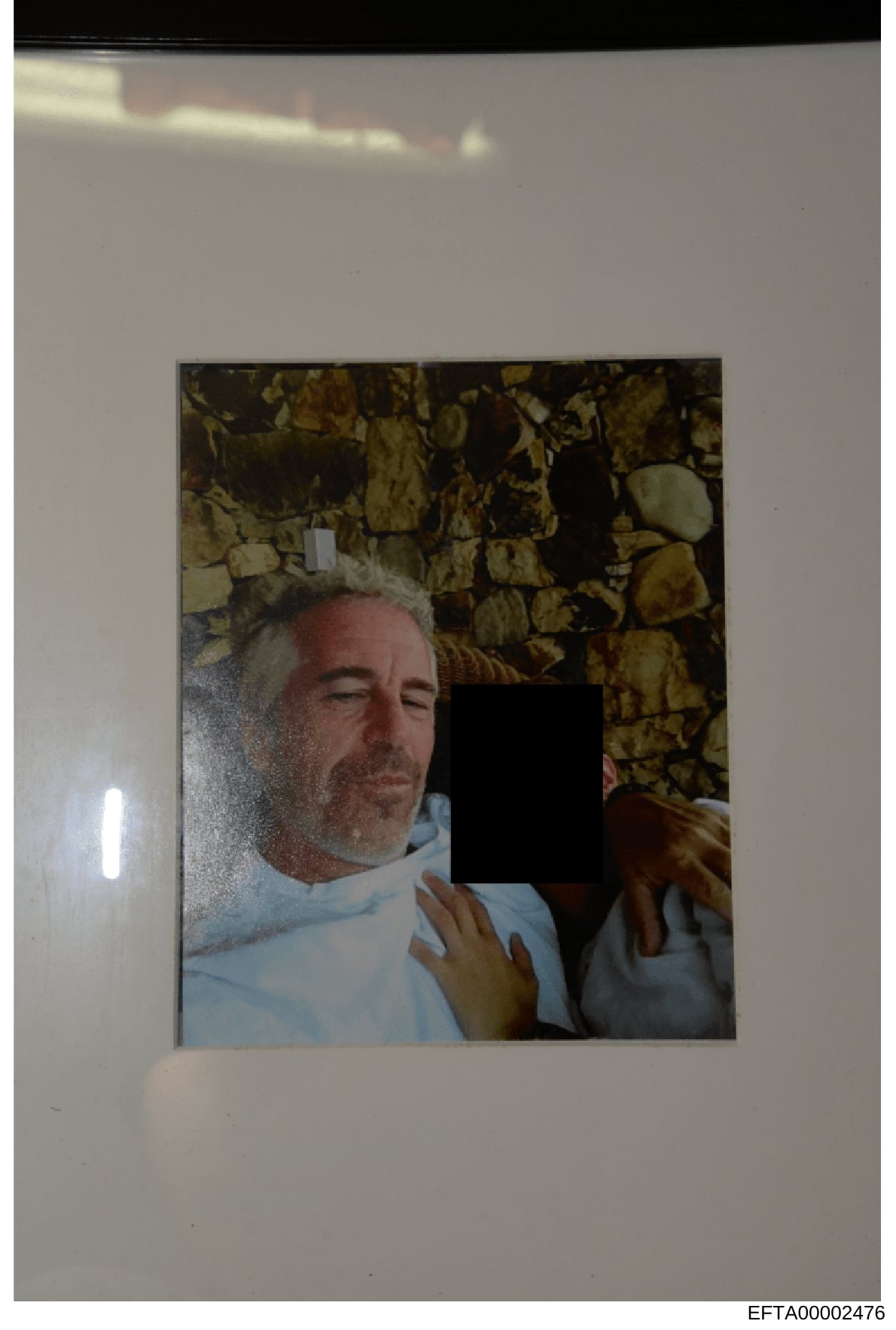 This is an evidence photograph showing a middle-aged male with gray/white hair wearing a light blue shirt, positioned against a stone or brick wall background. A portion of another person is visible on the right side of the frame, with their face red