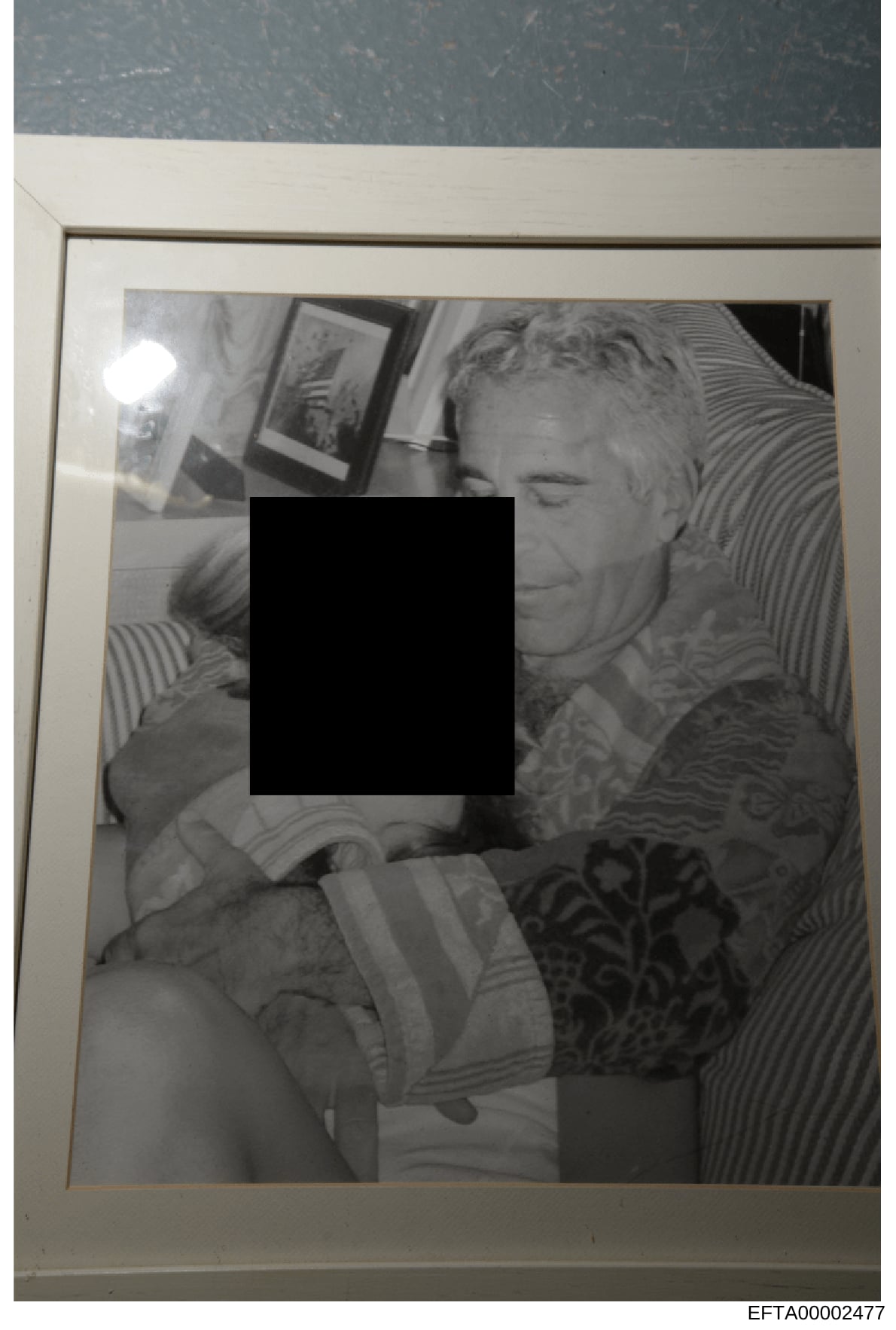 This is a black and white photograph that has been heavily redacted with a large black rectangle covering the central portion of the image. The visible portions show what appears to be an indoor domestic setting with framed artwork on walls and strip