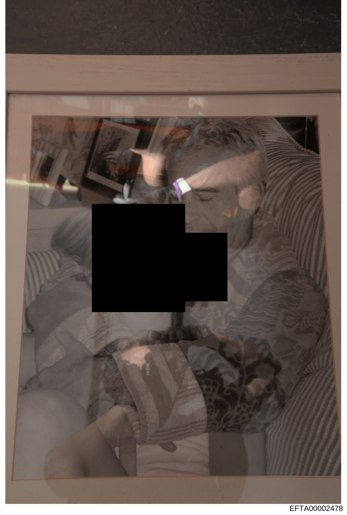 This is a photograph with significant redaction applied to the central portion. The image shows what appears to be an indoor setting with multiple people visible around the edges of the frame, though the primary content is obscured by a large black r