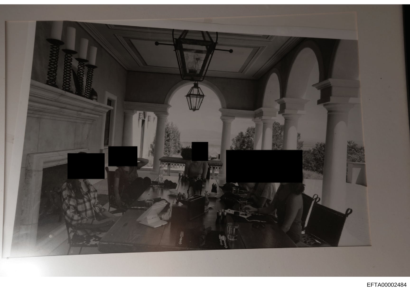 This black and white photograph shows the interior of an elegant, architecturally distinctive space featuring classical columns, arched doorways, and decorative lighting. Multiple individuals are present at what appears to be a dining table or gather