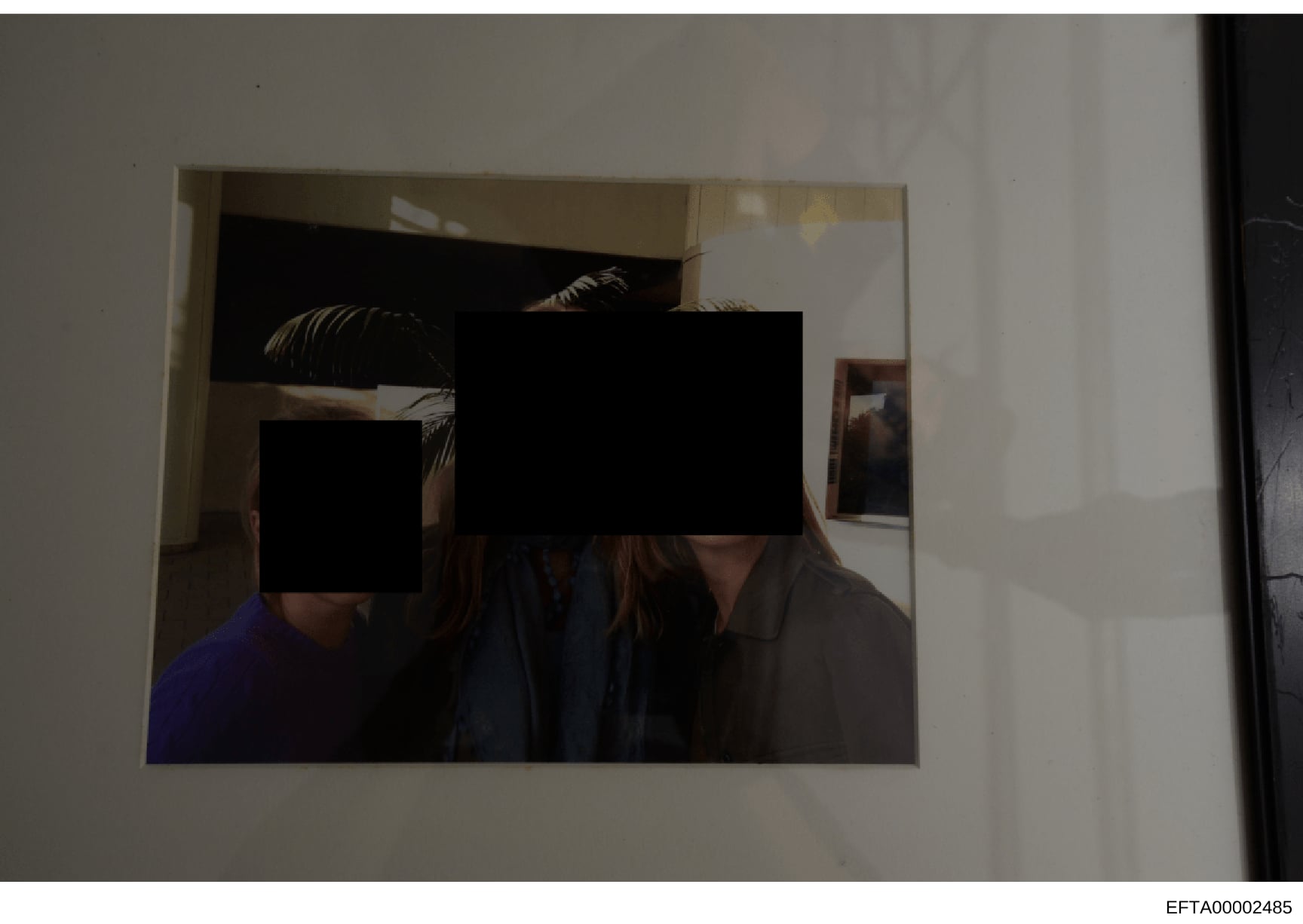This is a photograph of an interior room showing multiple individuals whose faces have been redacted with black rectangles. The setting appears to be a residential space with beige/tan walls, doorways, and decorative elements including framed artwork