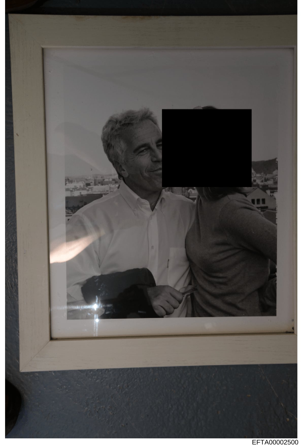 This is a black and white photograph showing two men at what appears to be a high-altitude location with a cityscape visible in the background. One man wears a white shirt and is clearly visible; the other man's face is redacted with a black rectangl