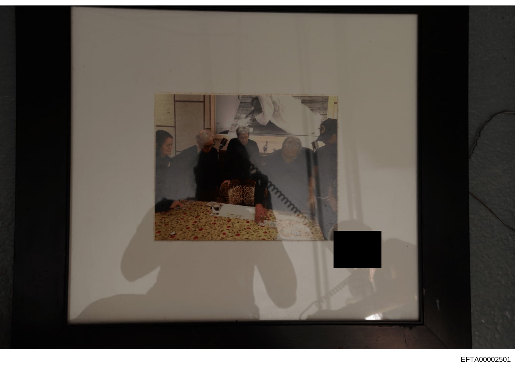 This is an evidence photograph depicting the interior of a residence with multiple people present in what appears to be a bedroom or living space. The image shows individuals gathered around a bed with patterned bedding. One figure in the lower right