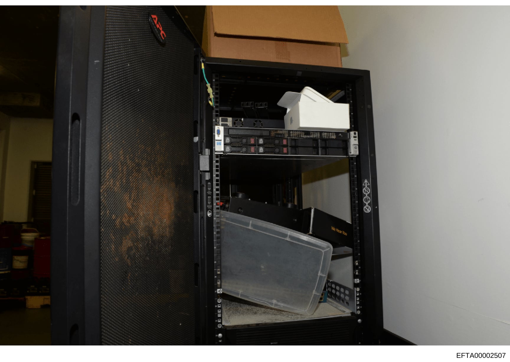 This is an evidence photograph showing the interior of a black server rack or equipment cabinet containing various networking and computing hardware, including server units with indicator lights, cables, and storage containers. The photo appears to b