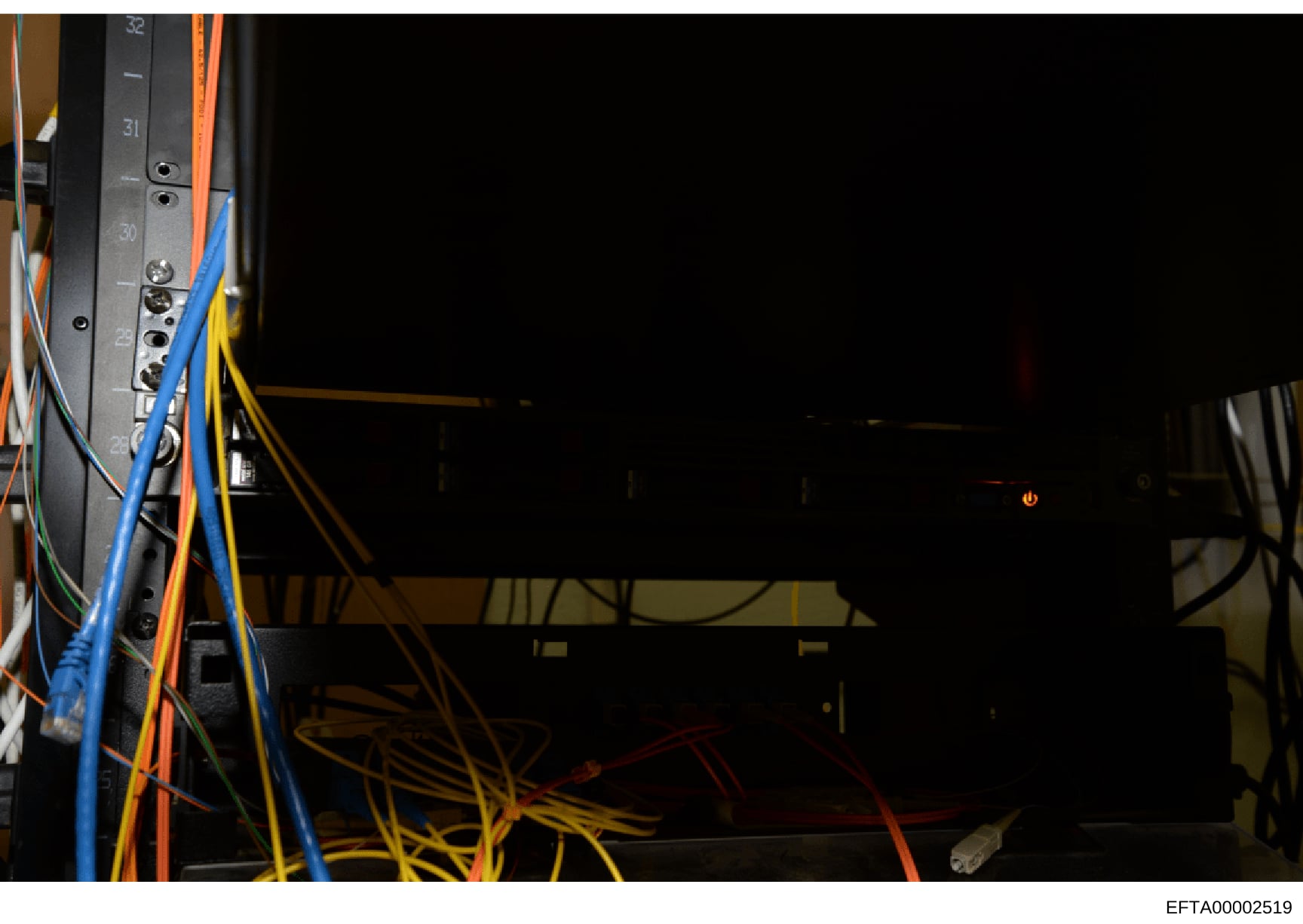 This is a photograph of electrical/networking equipment showing a server rack or panel with multiple colored wires (blue, orange, yellow, red, green) connected to numbered ports. The image appears to be documentation of infrastructure or equipment se