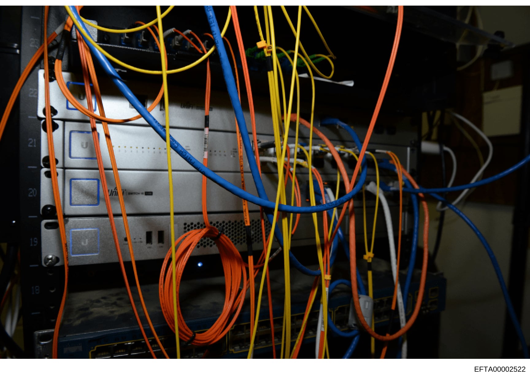 This is a photograph of server or network equipment showing multiple colored ethernet and power cables connected to a rack-mounted device with multiple port connections. The image appears to be evidence documentation related to digital infrastructure